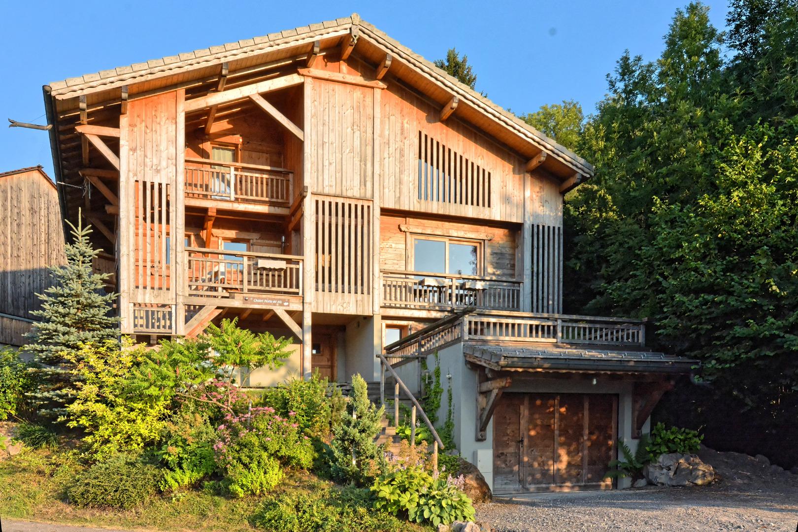 Le chalet en été au couchant. Vue des 3 niveaux du chalet et du garage qui contient le rangement des skis et une armoire sèche-chaussures.Porte motorisée. 