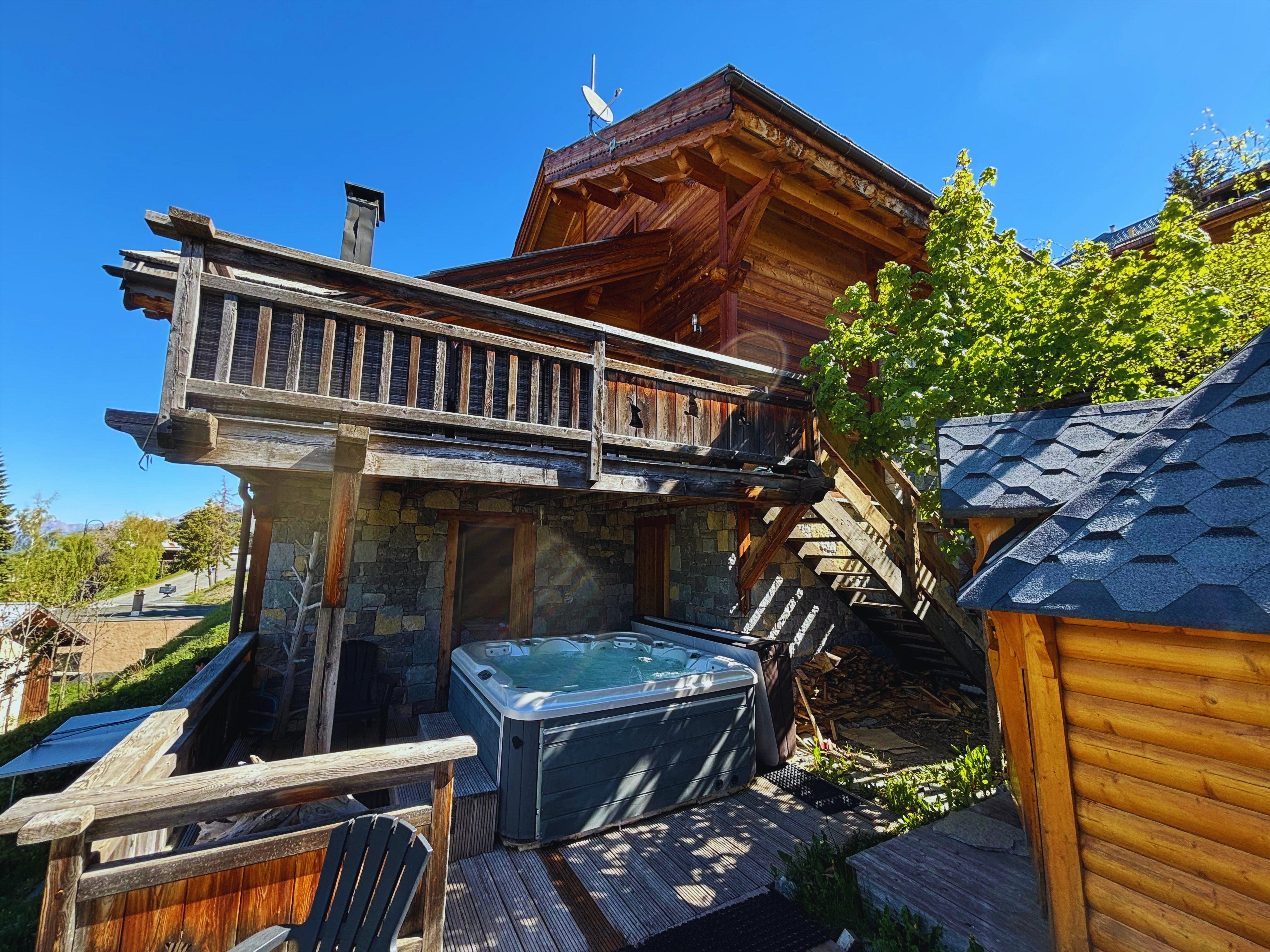 Chalet A Vars Sainte-Catherine — façade sud en bois et pierre avec jacuzzi extérieur et terrasse vue montagne