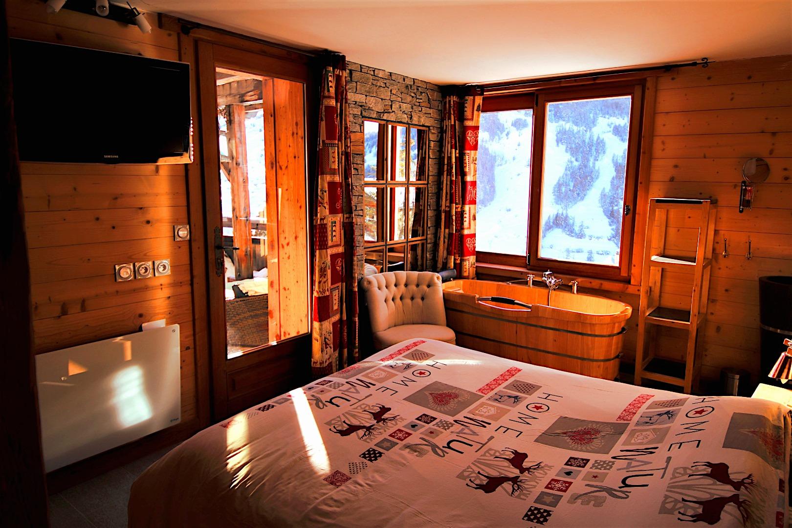  Chambre 2 avec baignoire en bois, murs en pierre et bois naturel, et vue dégagée sur les sommets des Hautes-Alpes — une suite intimiste dans un esprit chalet alpin authentique et haut de gamme